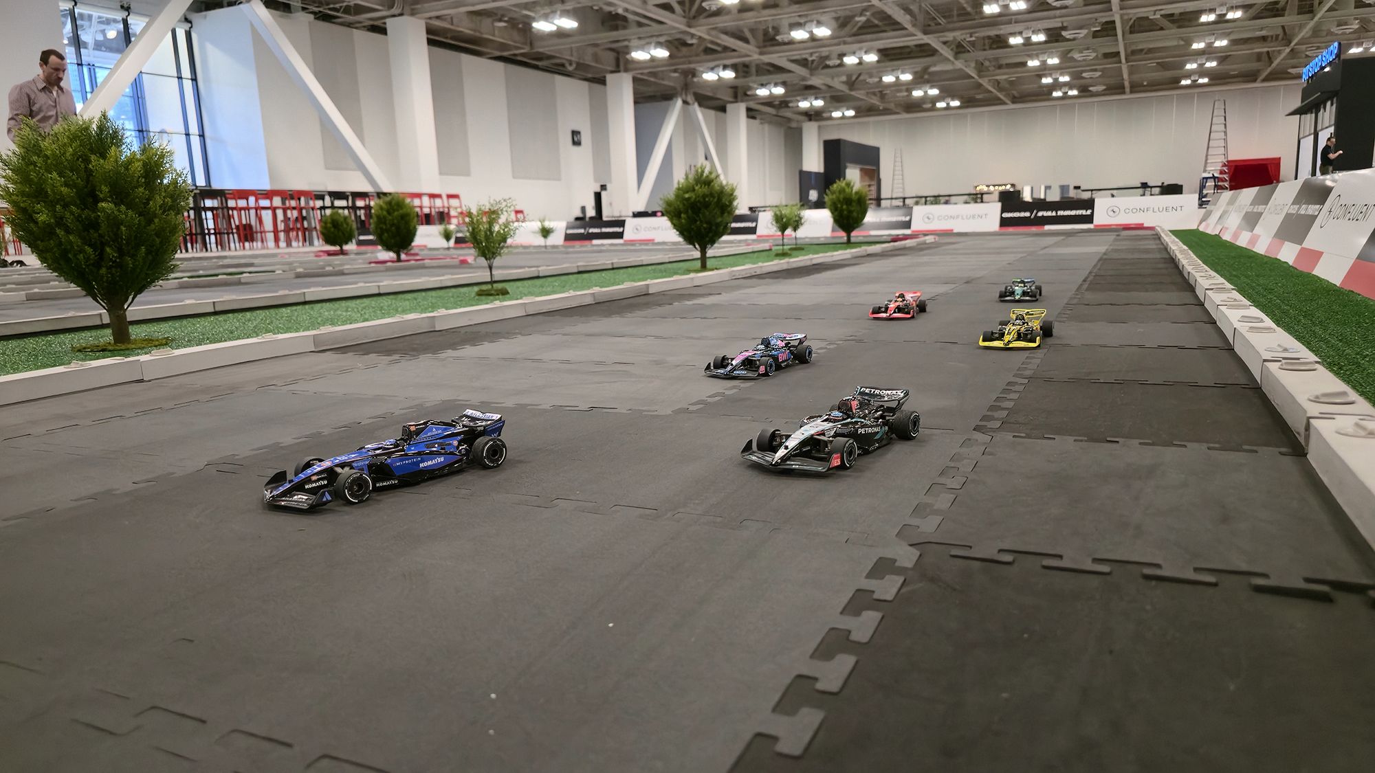 Immersive Formula 1 RC racing environment with turf, scale trees, and branded barriers