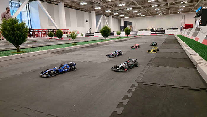 Immersive Formula 1 RC racing environment with turf, scale trees, and branded barriers