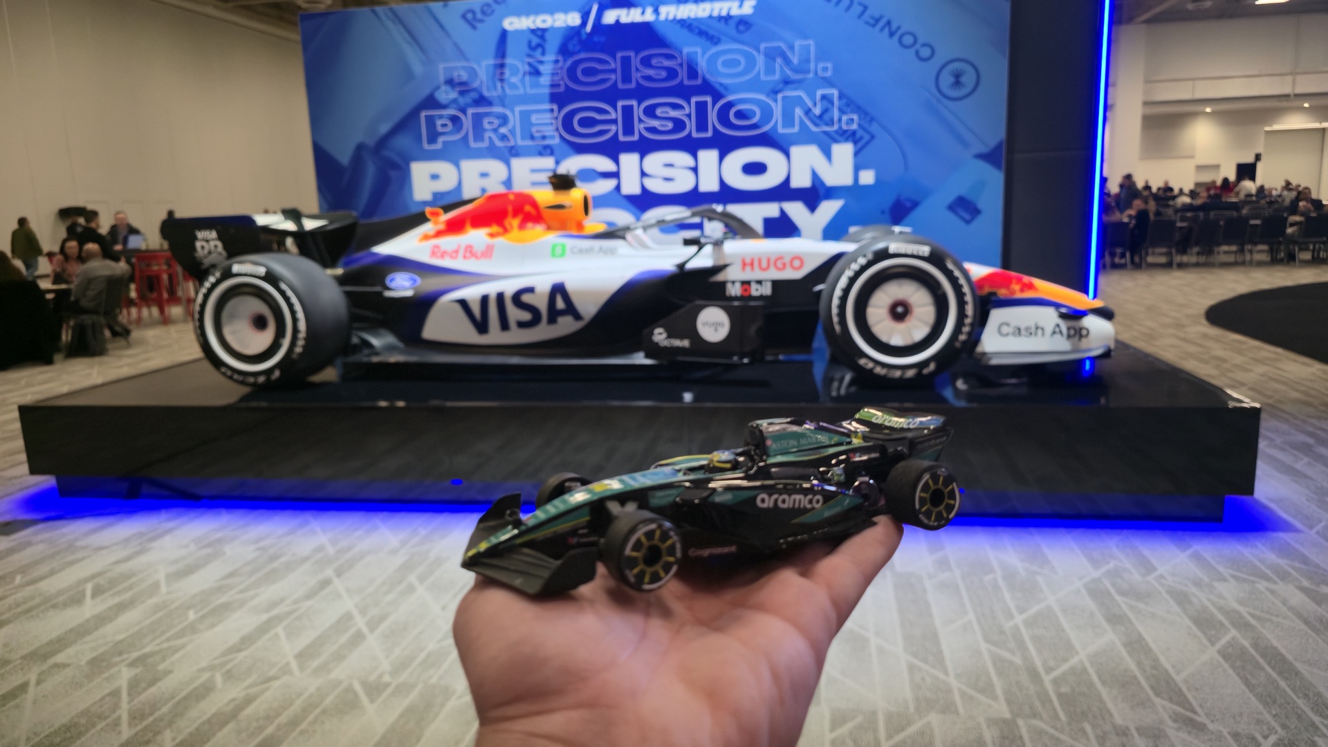 F1 replica RC car held beside a full-size Formula 1 show car